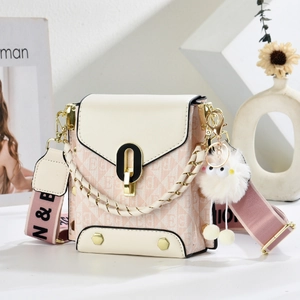 Detail of crossbody bag with gold U-lock, wide fabric strap, and plush ball charm