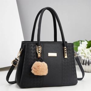 Detail of black quilted leather handbag with gold hardware and plush pom-pom charm