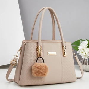 Detail of beige leather handbag with woven texture panels and brown faux fur pompom charm