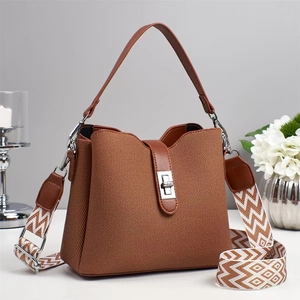 Detail of canvas bucket bag with leather trim, rotating metal lock and woven shoulder strap