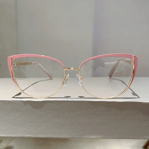 Detailed close-up of pink and gold cat-eye glasses frame with spring hinges on a platform
