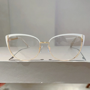 Close-up of cat-eye glasses with white frames and gold metal bridge on a neutral base