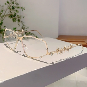 Detail der Y2K Sonnenbrille mit Goldrahmen und Strasssteinen auf weißem Sockel