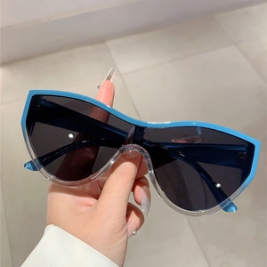 Detail of oversized shield sunglasses with blue and clear frame held by hand