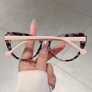 Detailed view of cat-eye eyewear showing tortoise front and pink temples held by hand
