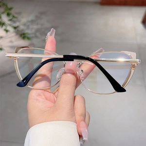 Close-up of stylish gold metal cat-eye frames with black temples held in hand