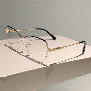 Detail of cat-eye metal glasses frame in gold and black on a minimalist display stand