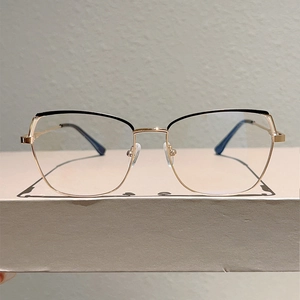 Detailed close-up of gold metal cat-eye eyeglass frame with black accent on upper rim
