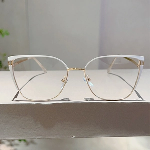 Detail of cat eye glasses with white acetate and gold metal frames on grey surface