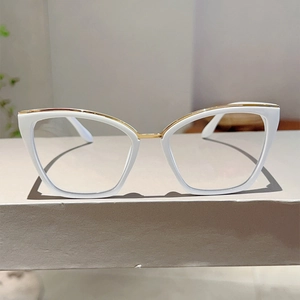 Detailed shot of ivory cat-eye glasses with golden metal accents on a gray display stand