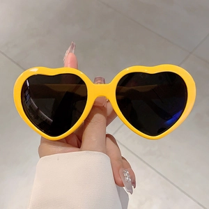 Gros plan d'une main tenant des lunettes de soleil coeur jaune pour la fête