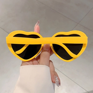 Détail de lunettes de soleil coeur jaune avec verres foncés tenues à la main pour fête