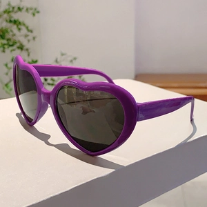 Vue détaillée de lunettes de soleil violettes en forme de cœur sur un support blanc