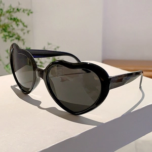 Détail de lunettes de soleil noires en forme de cœur avec verres foncés sur socle blanc