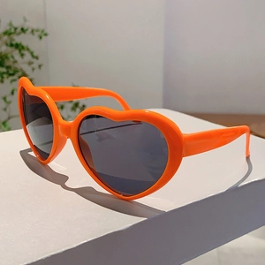 Détail de lunettes de soleil orange en forme de cœur avec verres foncés sur un support blanc