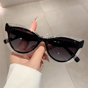 Detail of cat eye sunglasses with dual-layer black and glitter frame held by hand
