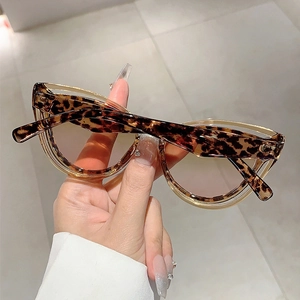 Close-up of leopard print cat-eye sunglasses with pink gradient lenses held by hand