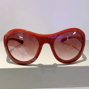 Detailansicht der roten Y2K-Sonnenbrille mit braunen Verlaufsgläsern auf weißem Sockel