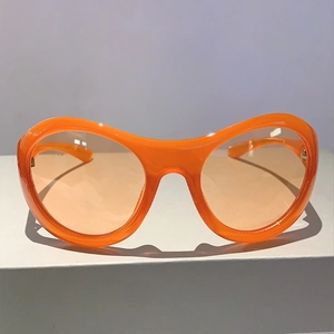 Nahaufnahme der orangefarbenen Y2K-Sonnenbrille mit Gläsern auf grauem Ständer