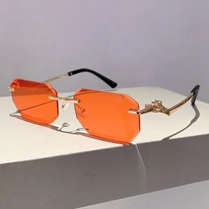 Detail of rimless octagonal sunglasses with orange lenses and golden leopard head hinges