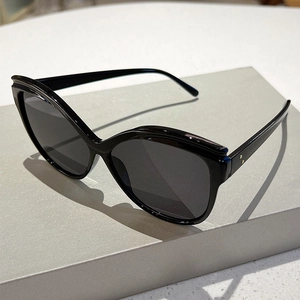 Close-up of black butterfly frame sunglasses featuring gold rivet details on simple gray stand