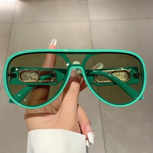 Detail of pilot sunglasses with green frames and oval gold decorative metal piece on temple