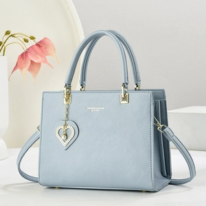 Light blue faux leather tote bag with heart charm and crossbody strap on white background
