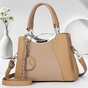 Classic khaki leather handbag with metal handles and tassel accent in minimalist setting