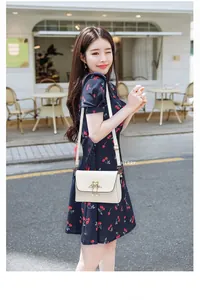 Close-up of white crossbody bag with gold swan buckle on a cherry print dress outfit