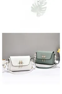 Detail of metal swan clasp and pearl tassel on beige and green faux leather bags