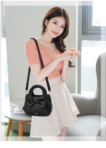 Detail of black crossbody bag with large bow and adjustable shoulder strap worn by model