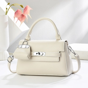 Detail of cream leather handbag featuring silver twist lock and mini charm accessory