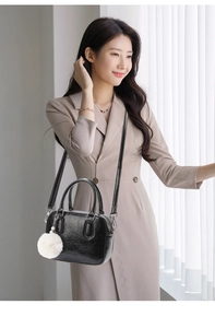 Detail of vintage black shiny pleated leather handbag with plush ball and metal hardware