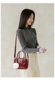 Deep red leather bowling bag with plush white charm shown in a lifestyle setting