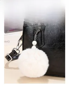 Close-up of a white faux fur ball charm with pearls on a black leather handbag