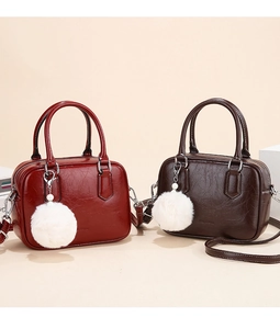 Close-up of pleated leather texture on dark burgundy and coffee crossbody bags with fur balls