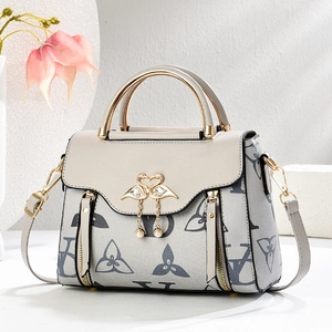 Chic monogram crossbody bag with golden swan clasp and pearl detail on a floral display