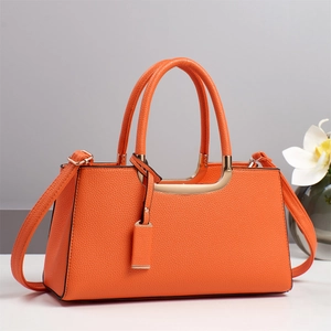Détail d'un sac à main orange en cuir grainé avec poignées et finitions métalliques dorées