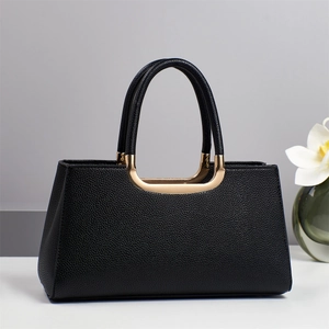Détail d'un sac à main en cuir noir avec une poignée élégante en métal doré incurvé