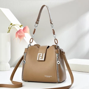 Brown leather crossbody bag with top handle and gold geometric logo on white pedestal