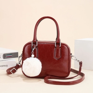 Polished burgundy bowling handbag with white pompom charm and detachable shoulder strap