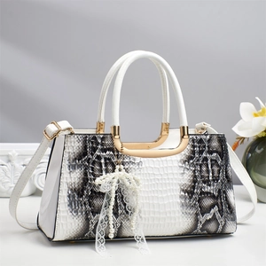 Close-up of white snakeskin texture handbag with gold hardware and pearl bow charm