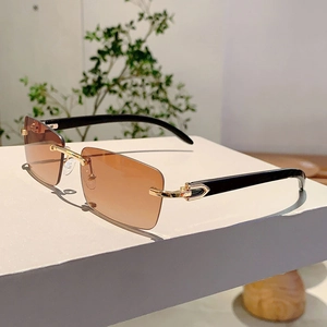 Detail of rimless sunglasses featuring brown gradient lenses and golden C-shaped hinges
