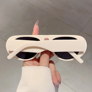 Detail of cream oval sunglasses with thick frames and dark UV protection lenses