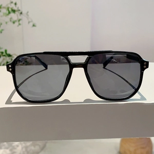 Close-up of black navigator sunglasses with dual silver rivets on a white display pedestal