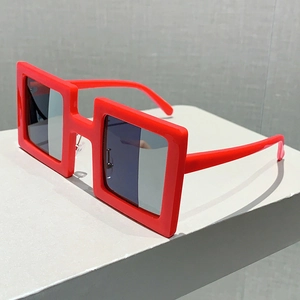 Detail shot of oversized red square frame sunglasses with dark lenses on a white pedestal