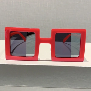 Close-up of red square frame sunglasses with dark lenses on a minimalist pedestal