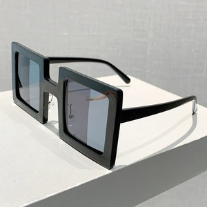 Detail of square black sunglasses with blue lenses on a minimalist white pedestal display