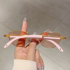 Detailed close-up of oval sunglasses with gold metal frame and light pink temples