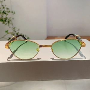 Detail of gold metal cat-eye sunglasses with green gradient lenses on a minimalist stand